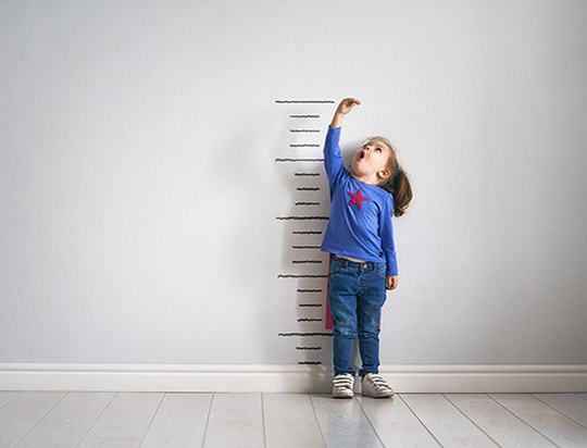 une petite fille mesure sa croissance adossée à un mur